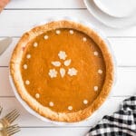 Overhead view of a whole sweet potato pie with white plates and forks on the table.