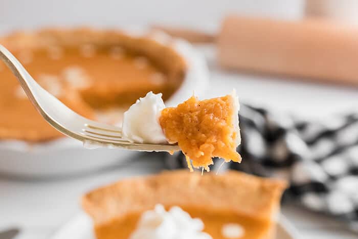 A fork holding a bite of sweet potato pie and whipped cream.