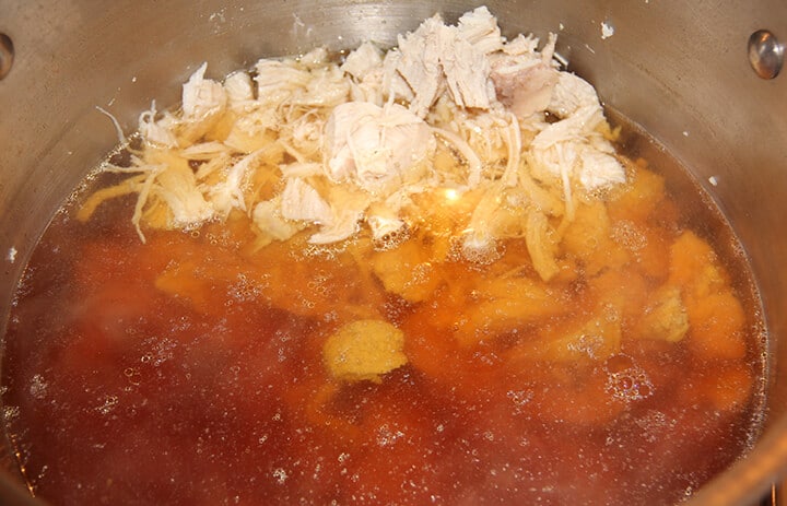 Chopped chicken in a stainless pot of stock.