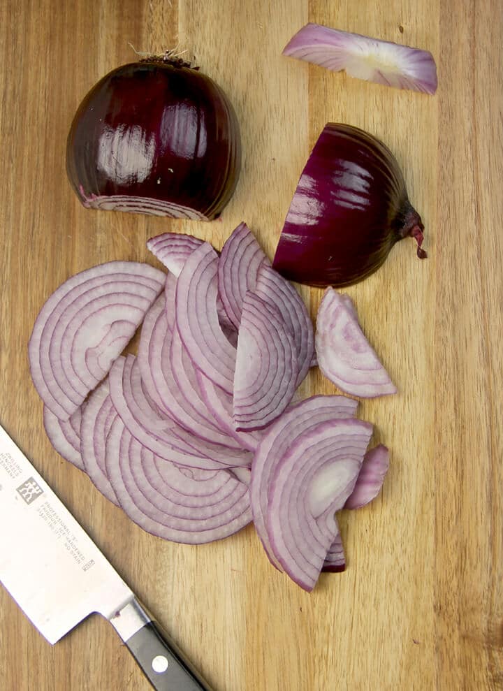 Sliced red onions on a cutting board next to a knife.