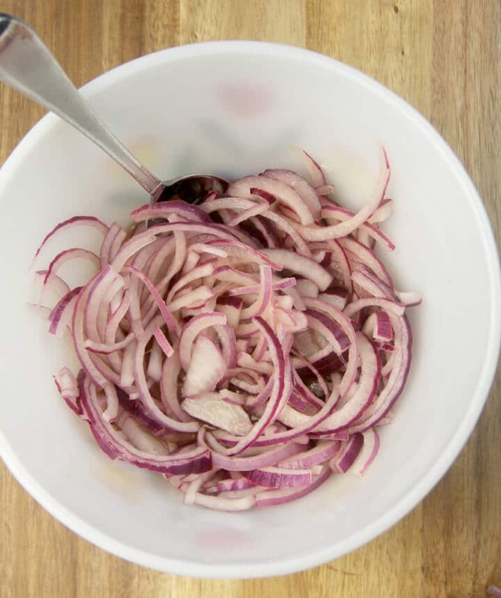 Red onions sliced in a bowl on a wood board.
