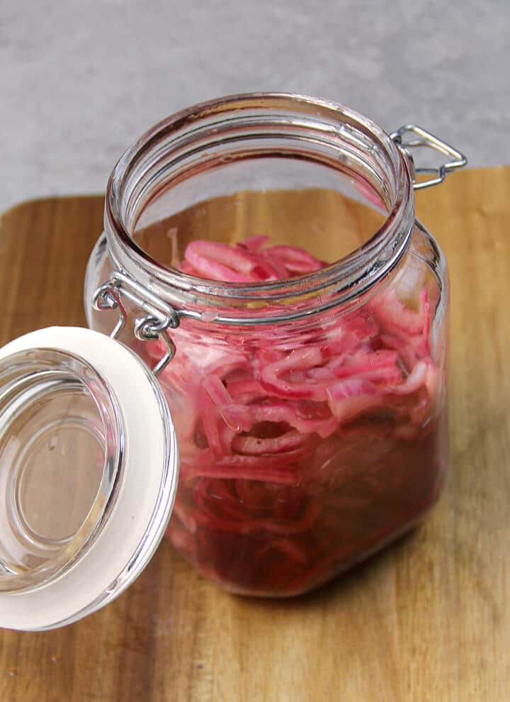 A jar of pickled red onions on a wooden cutting board.