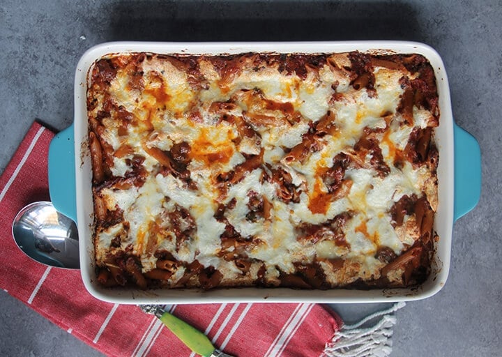 A blue baking dish filled with pasta bake with chicken on a red striped towel with a spoon.