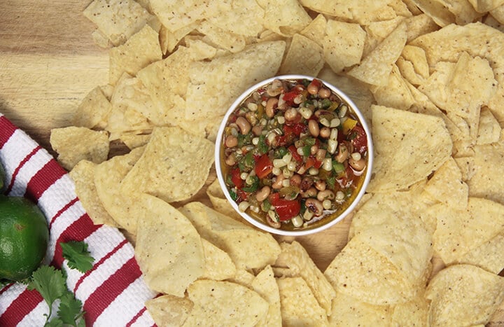 Tortilla chips on a board with a white bowl of cowboy caviar.