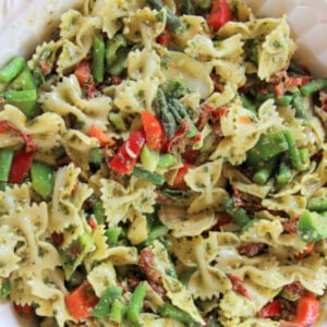 A bowl of pesto pasta salad with lemon basil pesto salad dressing, along with bowtie pasta, sundried tomatoes, asparagus, artichoke hearts, and more lemon zest.