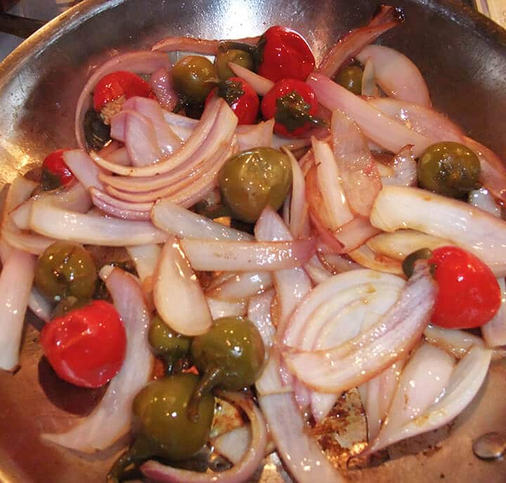 Cherry peppers and onions in a skillet.