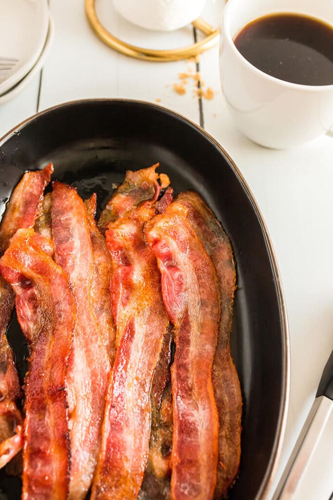 Closeup photo of oven baked bacon on a black platter.