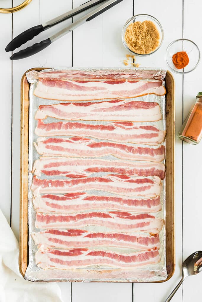 A sheet pan of raw bacon slices ready to cook.