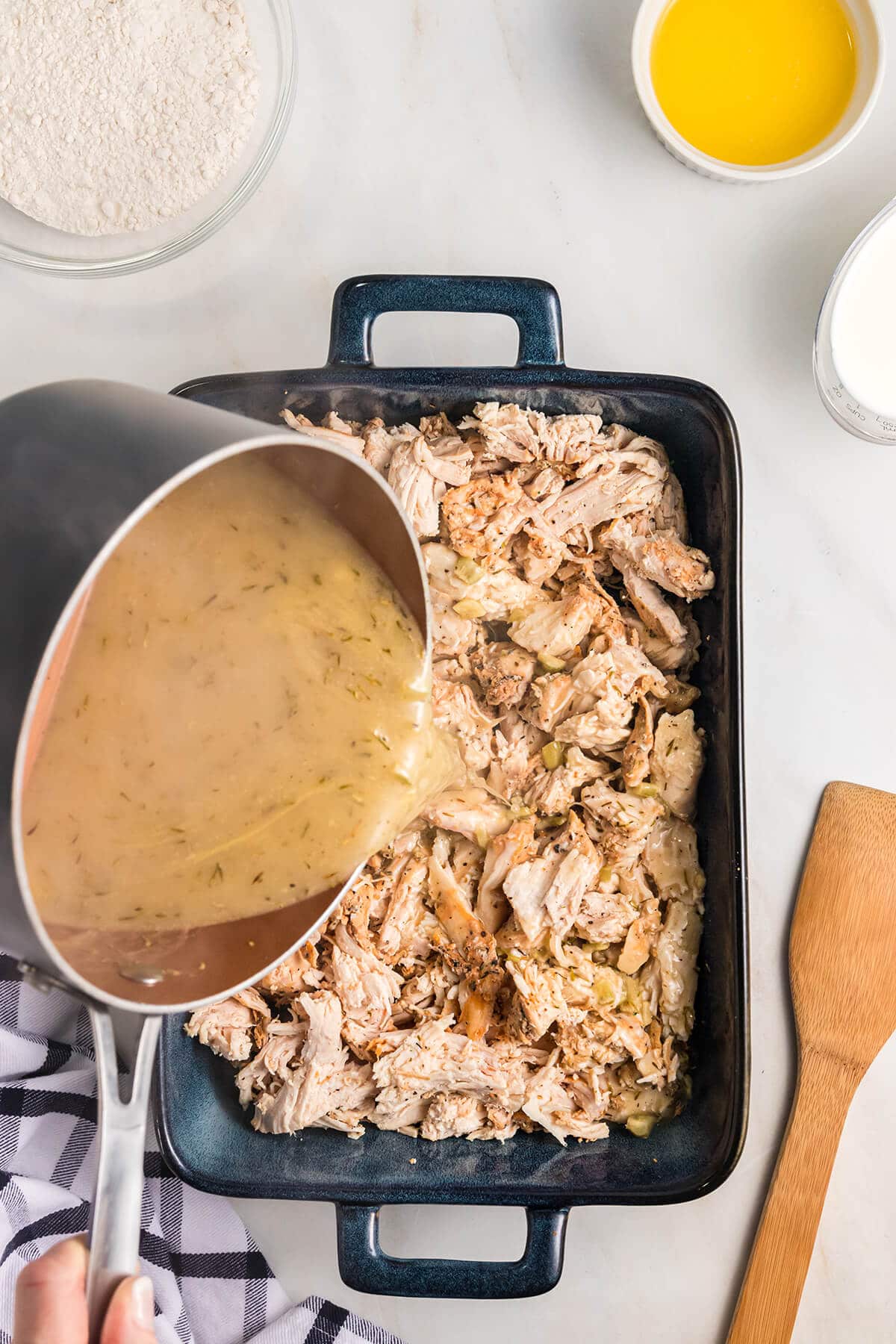 Pouring broth onto shredded chicken in a baking dish.