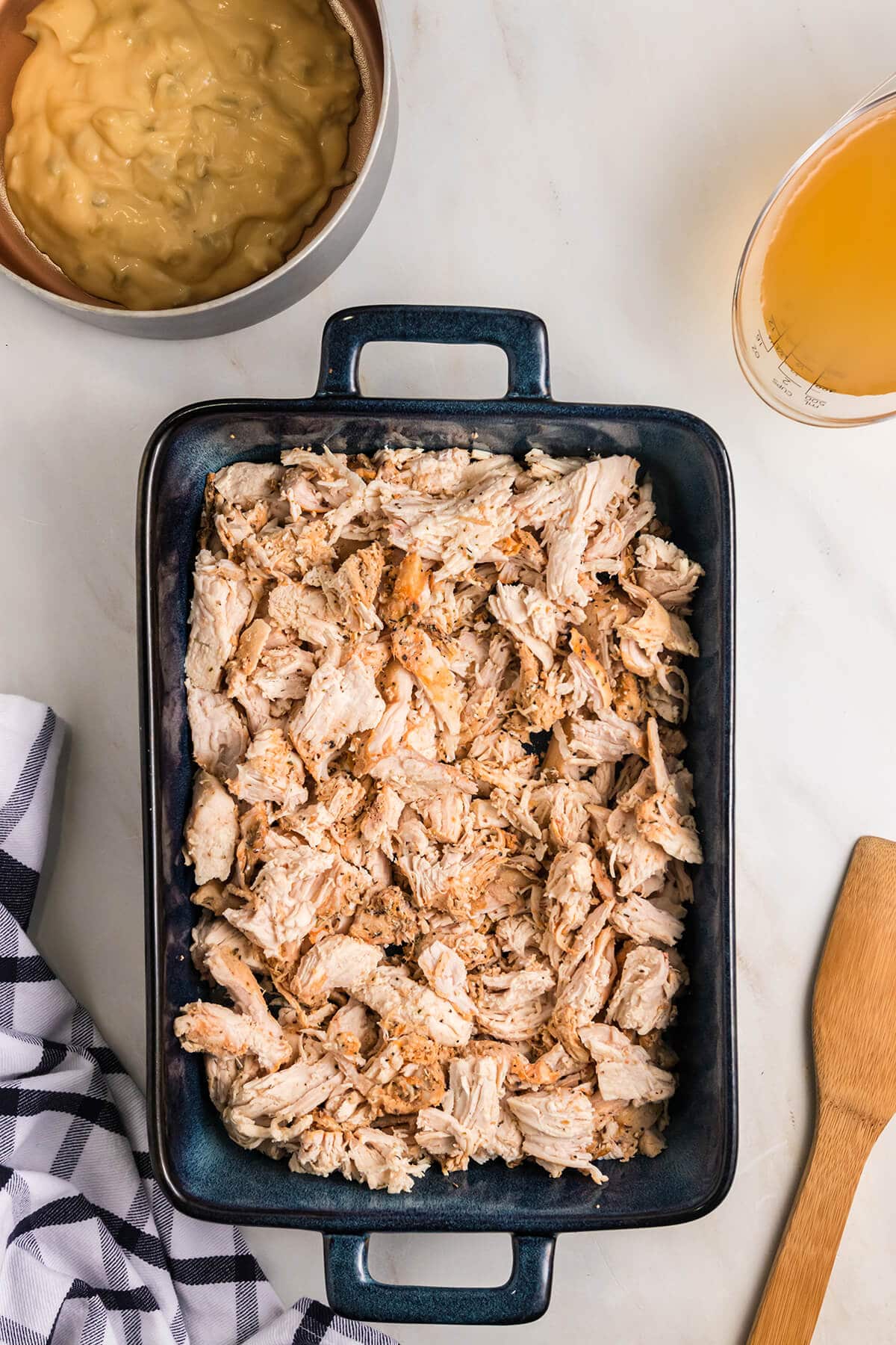 Shredded chicken in a baking dish with a wooden spoon on the side.