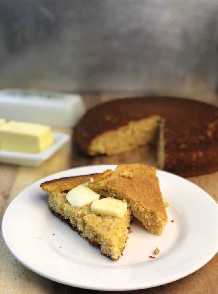 A slice of southern cornbread with melting butter on a white plate.