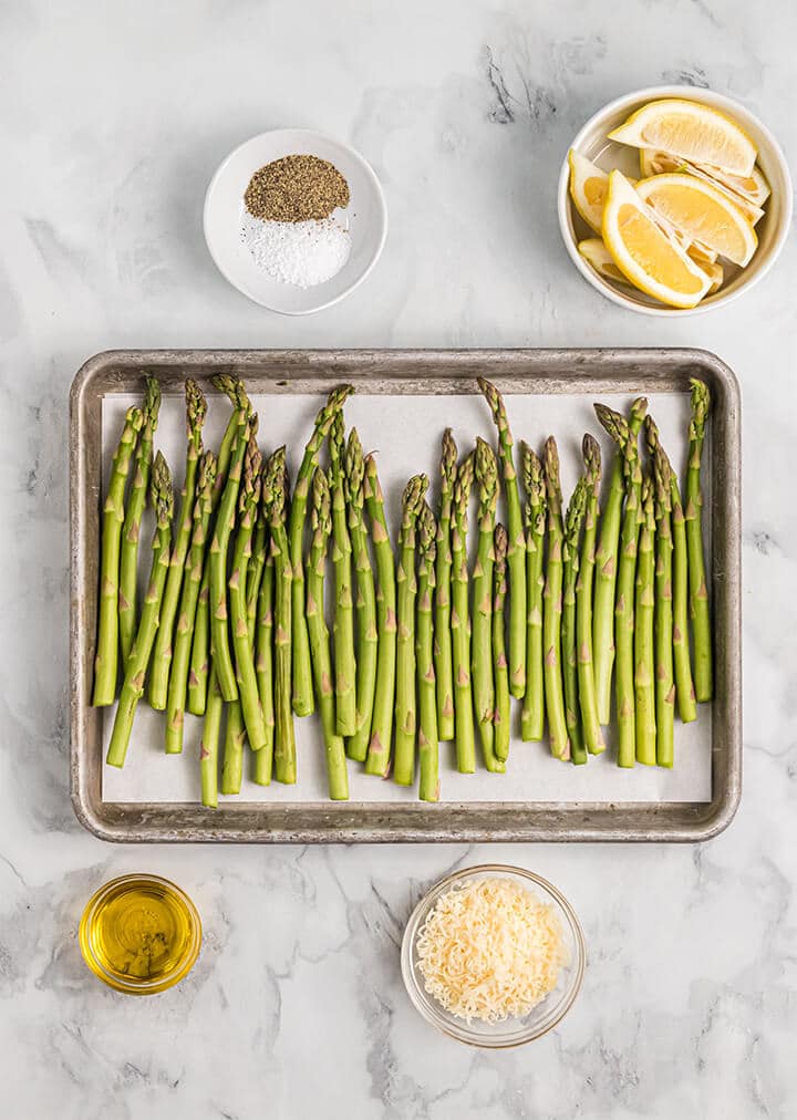 Asparagus stalks on a baking sheet with olive oil and cheese.