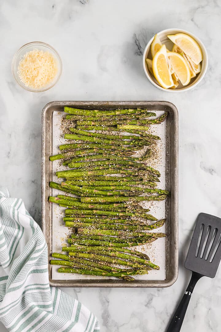 Asparagus with salt and pepper on baking sheet.