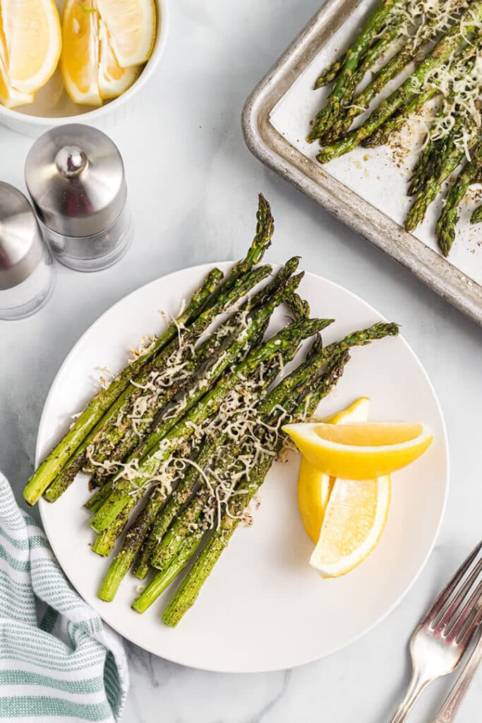 Roasted asparagus parmesan on a white plate with a fork on the side.
