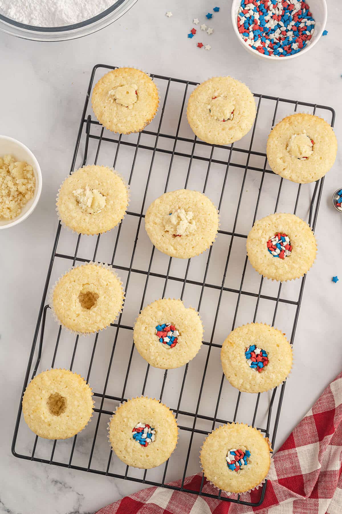 Cupcakes on a cooling rack with holes filled with sprinkles.