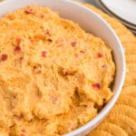 Closeup of a white bowl filled with pimento cheese surrounded by ritz crackers.