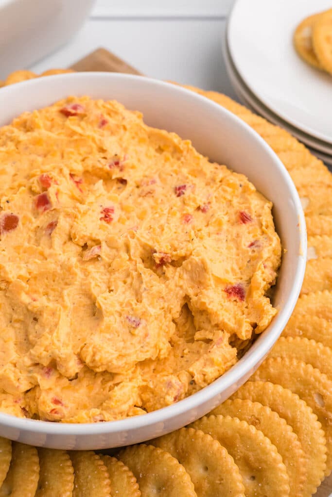 Closeup of a white bowl filled with dip and surrounded by ritz crackers.