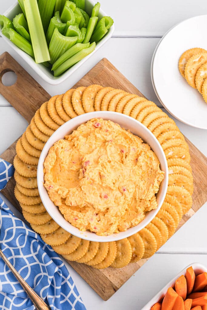 Pimento cheese in a white bowl on a cutting board with Ritz crackers.