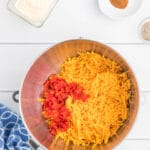 A stainless steel mixing bowl filled with grated cheese and red pimentos.