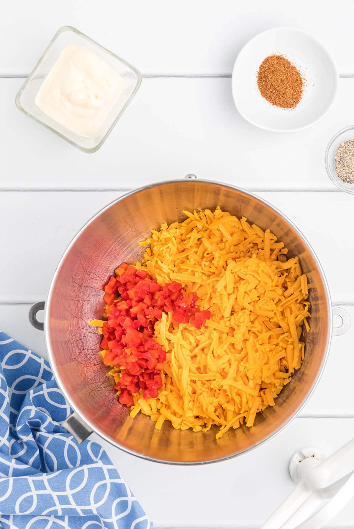 A stainless steel mixing bowl filled with grated cheese and red pimentos.