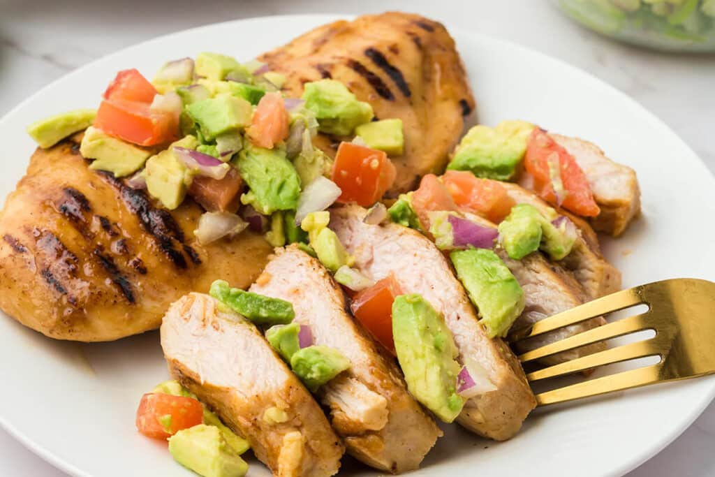 white plate with grilled chicken topped with avocado salsa
