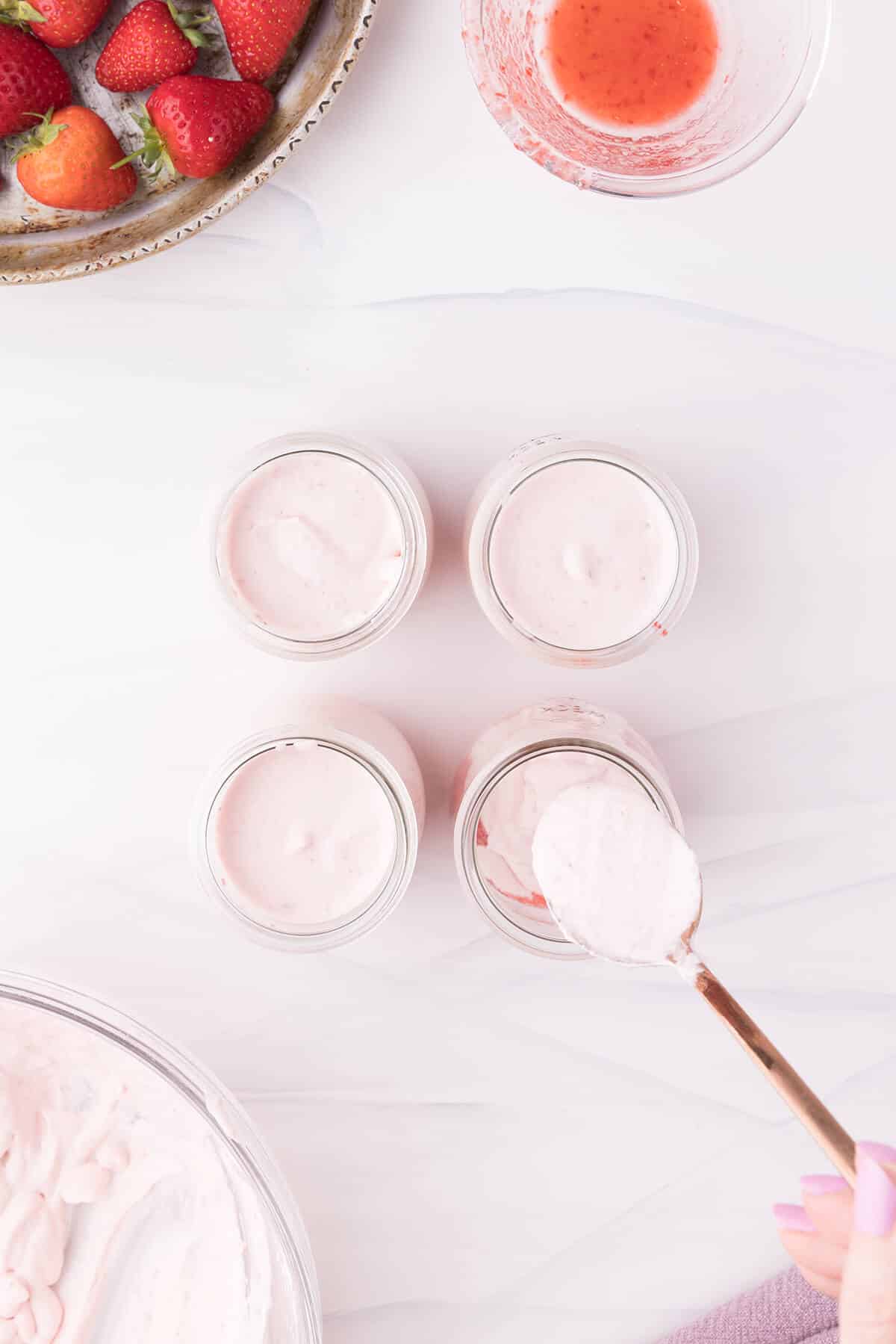 Adding the whipped strawberry cream to the glass jars.