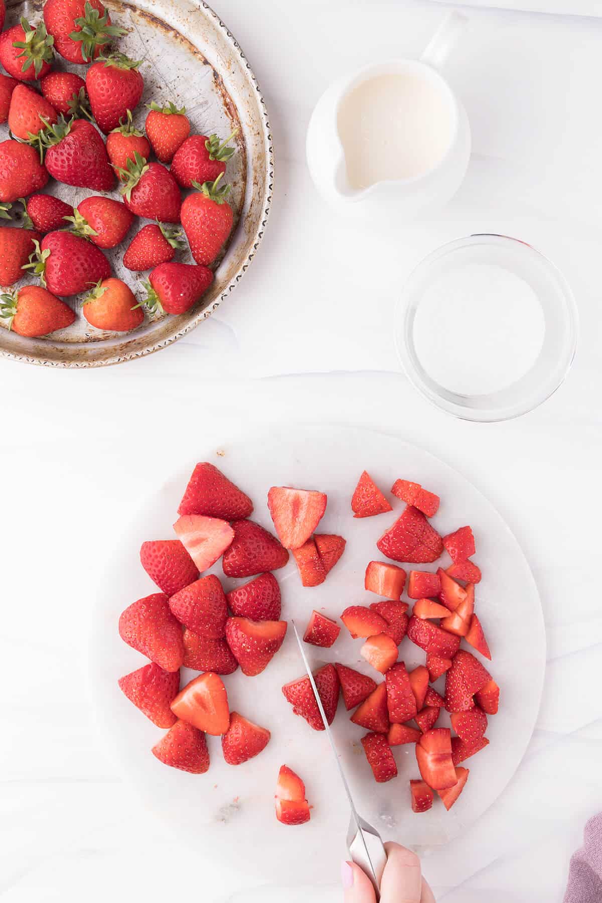 Plate filled with fresh strawberries and a chopping board with strawberries being chopped.