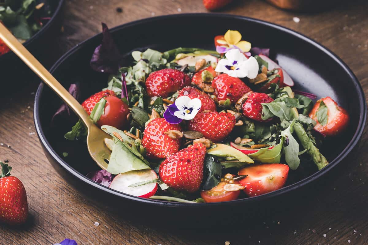 bowl full of salad greens topped with fresh strawberries