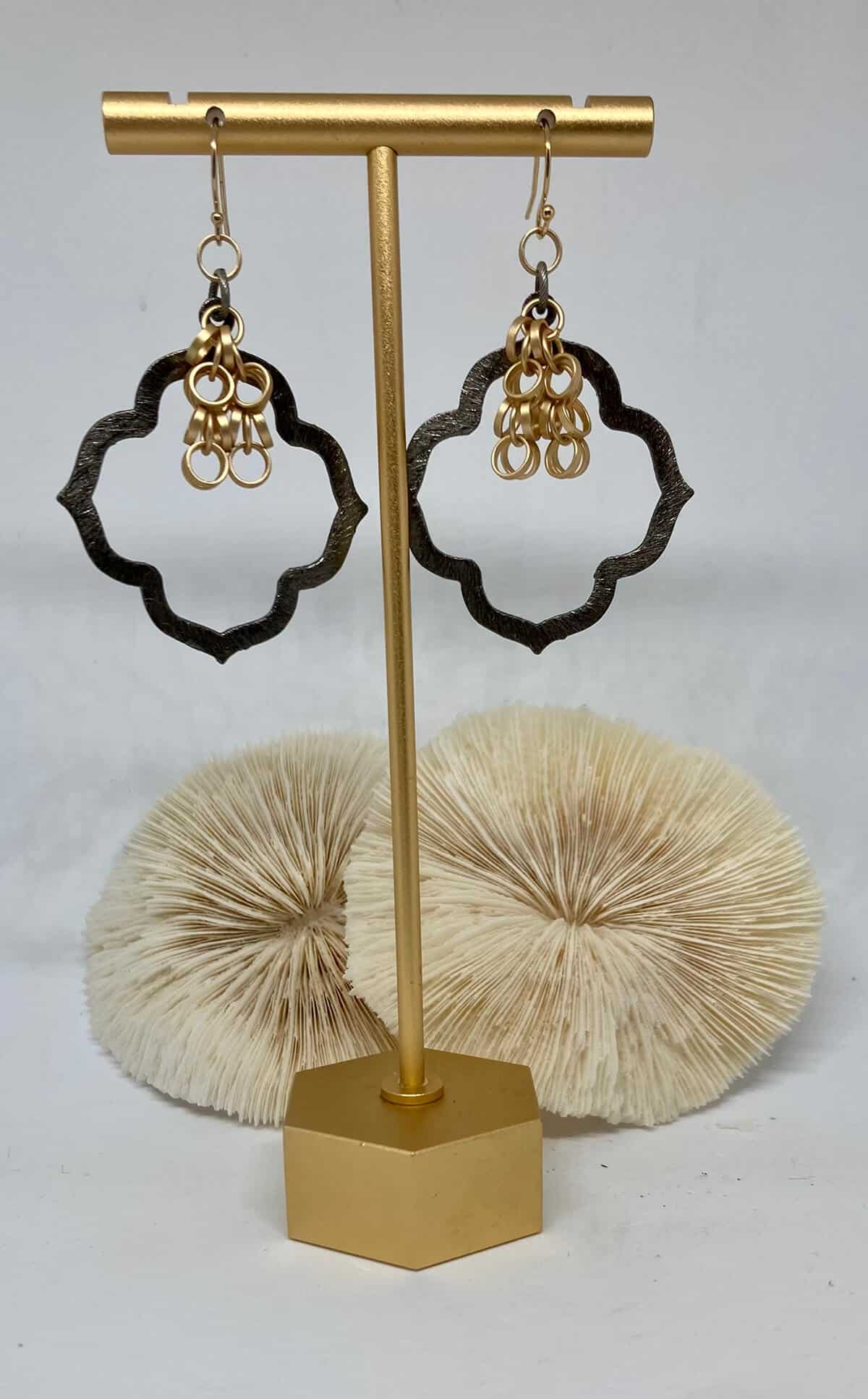 Black and gold earrings on a gold stand with white shells in the background.