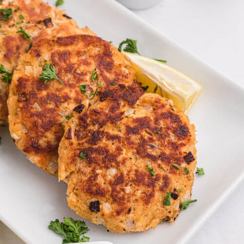 three salmon burgers stacked on a white platter