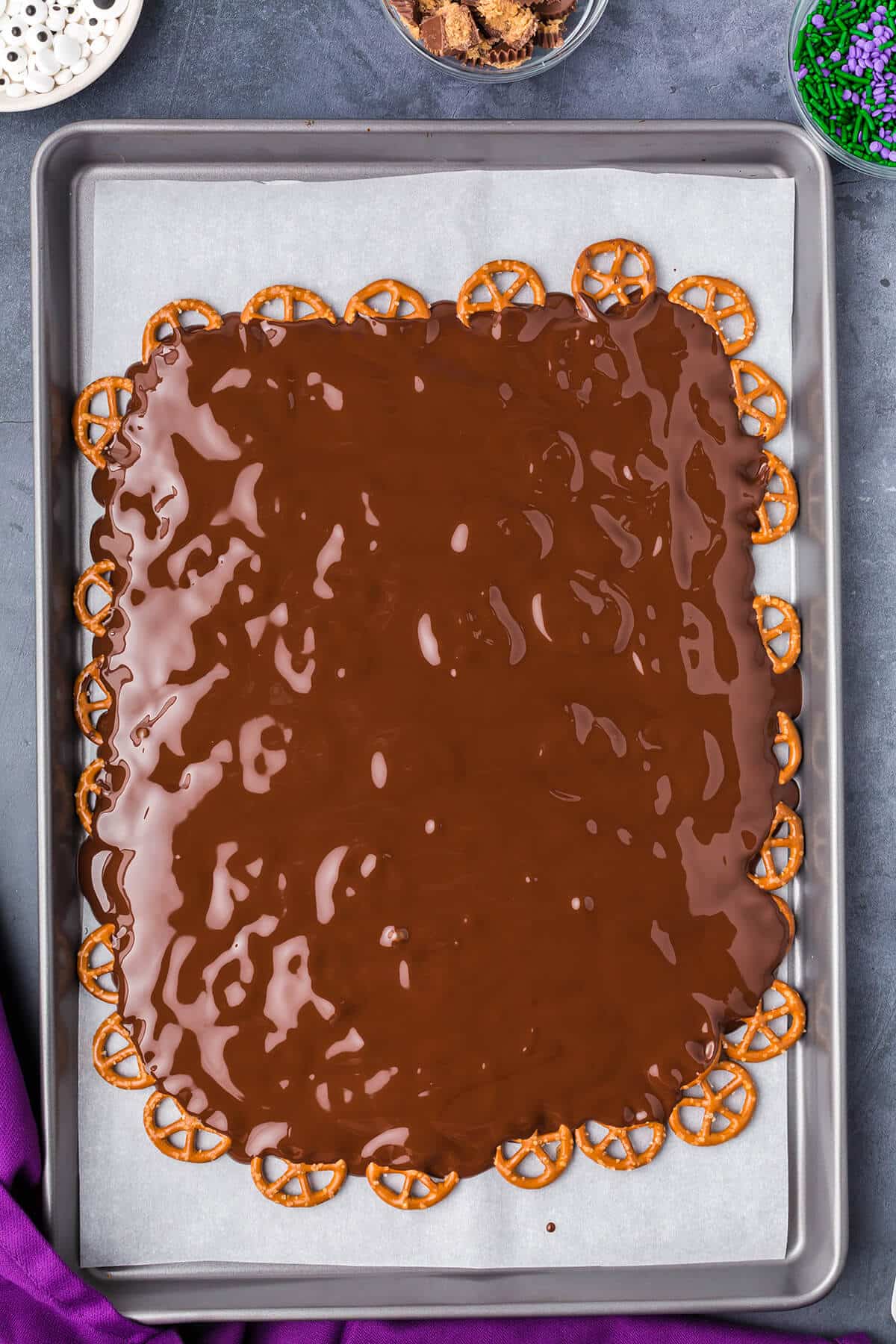melted chocolate poured over pretzels on a baking sheet