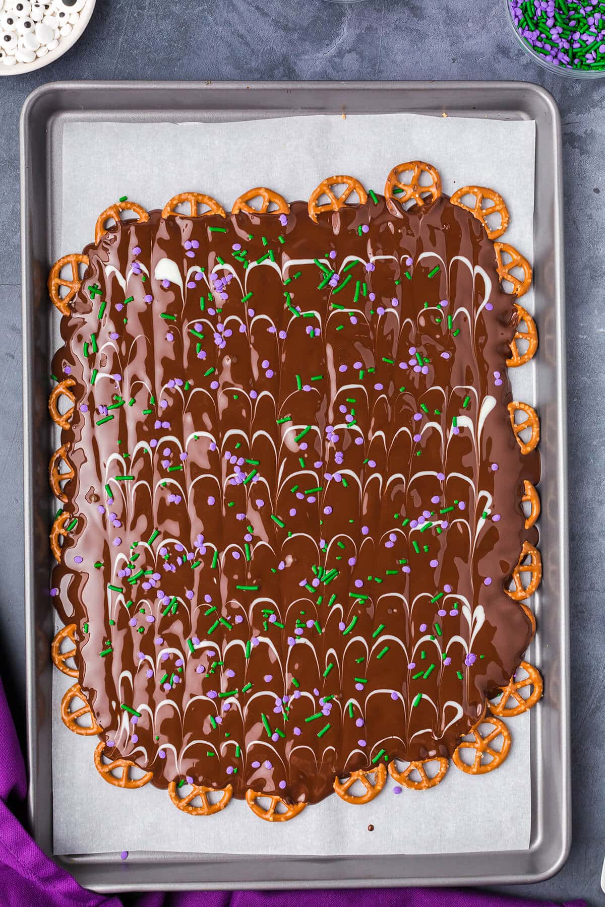 purple and green sprinkles over pretzel bark on a baking sheet