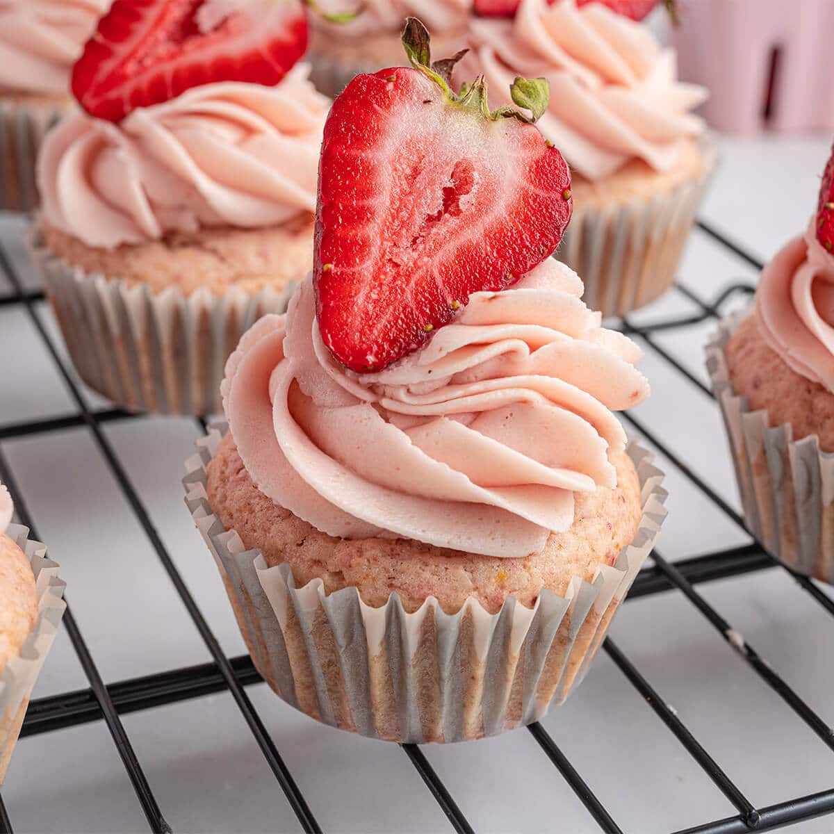 A close up of a strawberry cupcake with frosting and fresh strawberry.