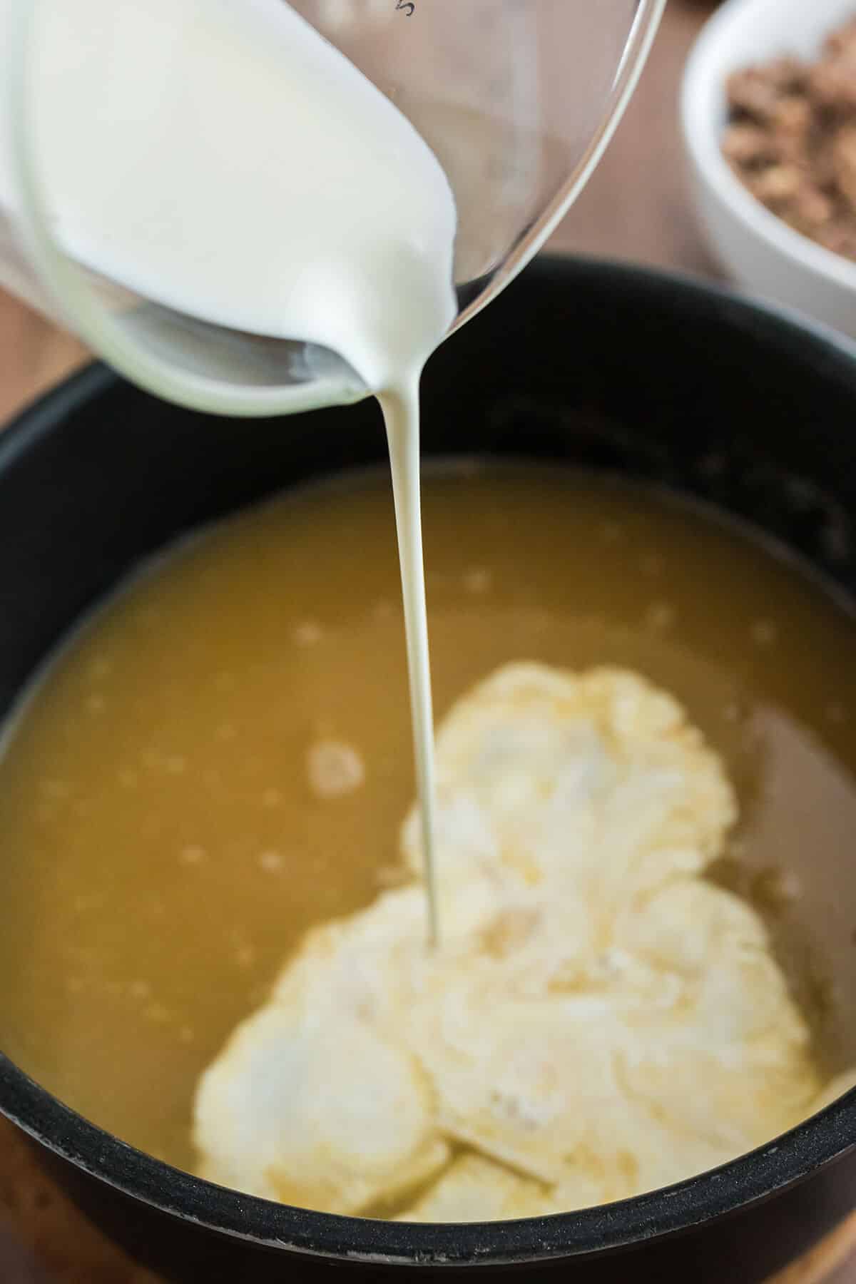 Pouring heavy cream into a pot of stock.
