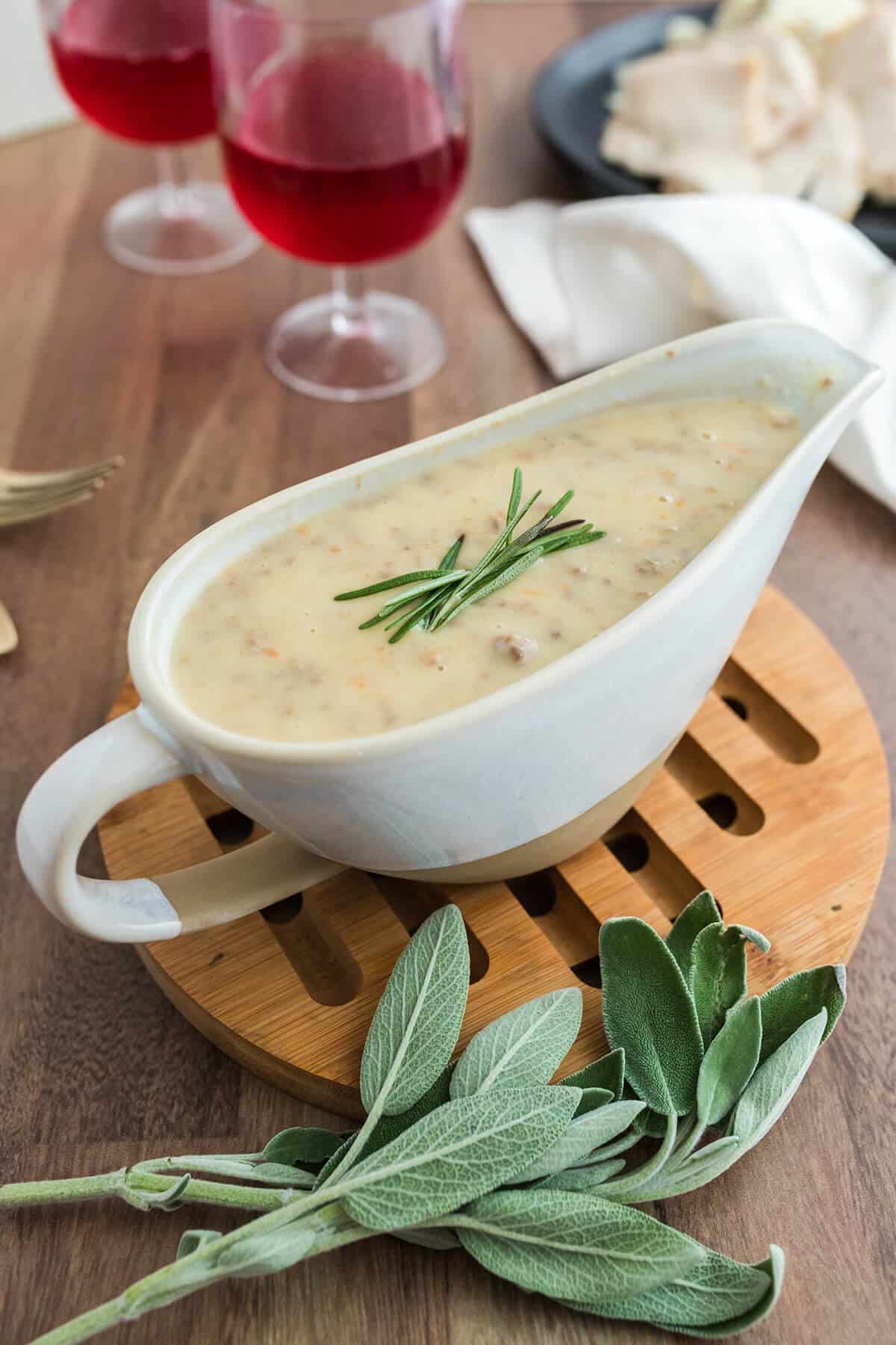 A gravy boat filled with giblet gravy with fresh sage on the counter.