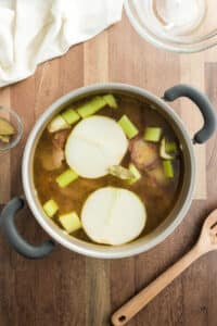 A pot of stock on the counter with an onion and a wooden spoon.