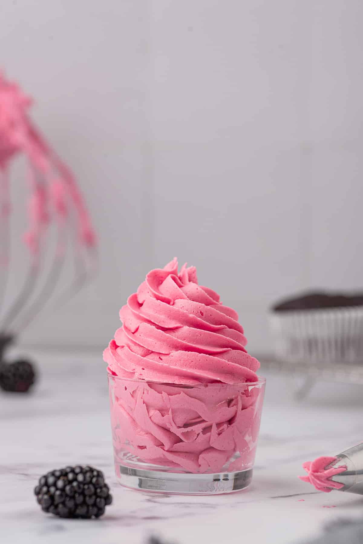 A glass filled with pink blackberry buttercream frosting.