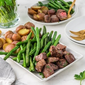 a white plate with steak bites and green beans.