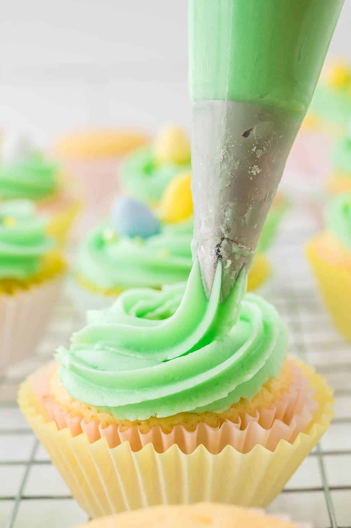 Piping green buttercream frosting on cupcakes.