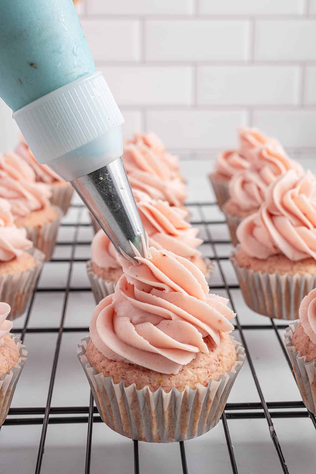 Piping strawberry buttercream frosting on a cupcake.