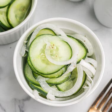 Small white bowl filled with cucumbers and onions in vinegar.