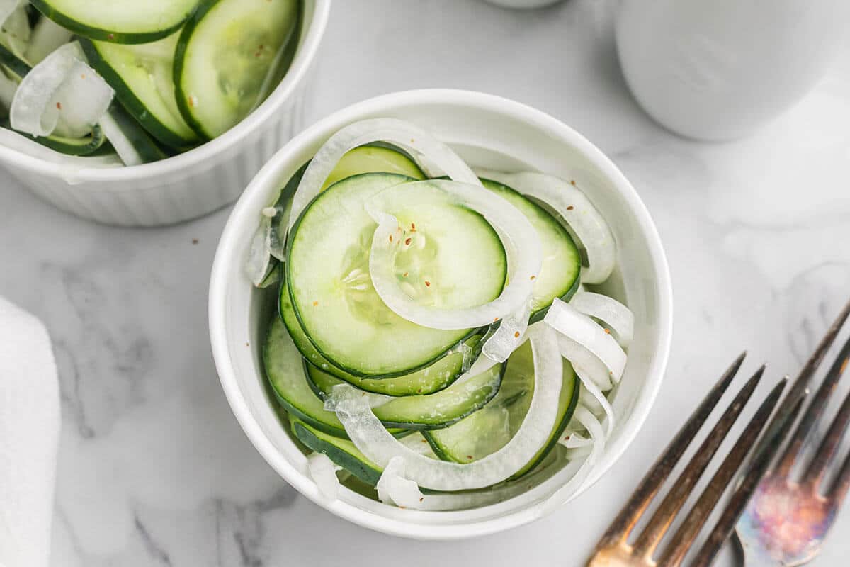 Small white bowl filled with cucumbers and onions in vinegar.