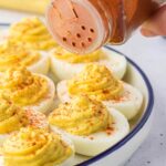 Sprinkling paprika over deviled eggs.