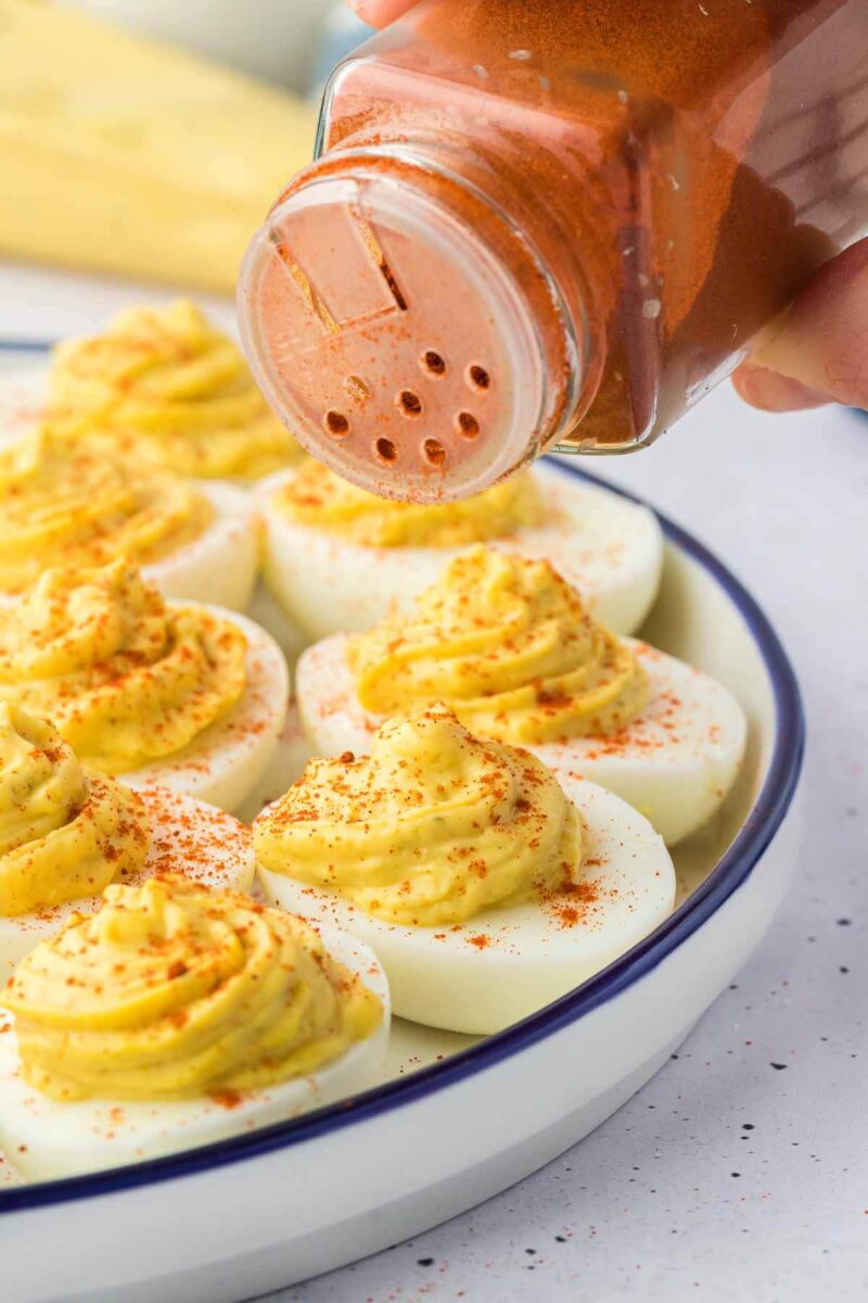Sprinkling paprika over deviled eggs.