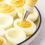 Pastry bag piping deviled egg filling into the white halves.