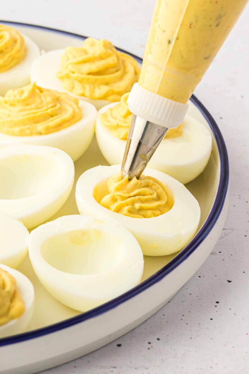 Pastry bag piping deviled egg filling into the white halves.