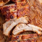 Oven baked ribs in foil on a cutting board.