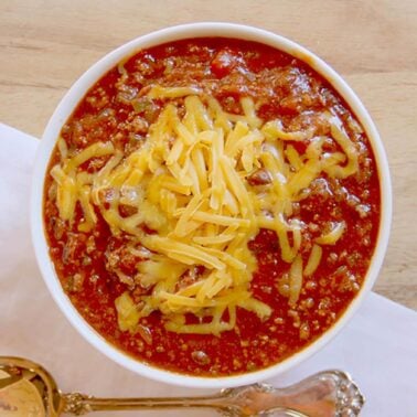 A bowl of beef chili topped with grated cheese.