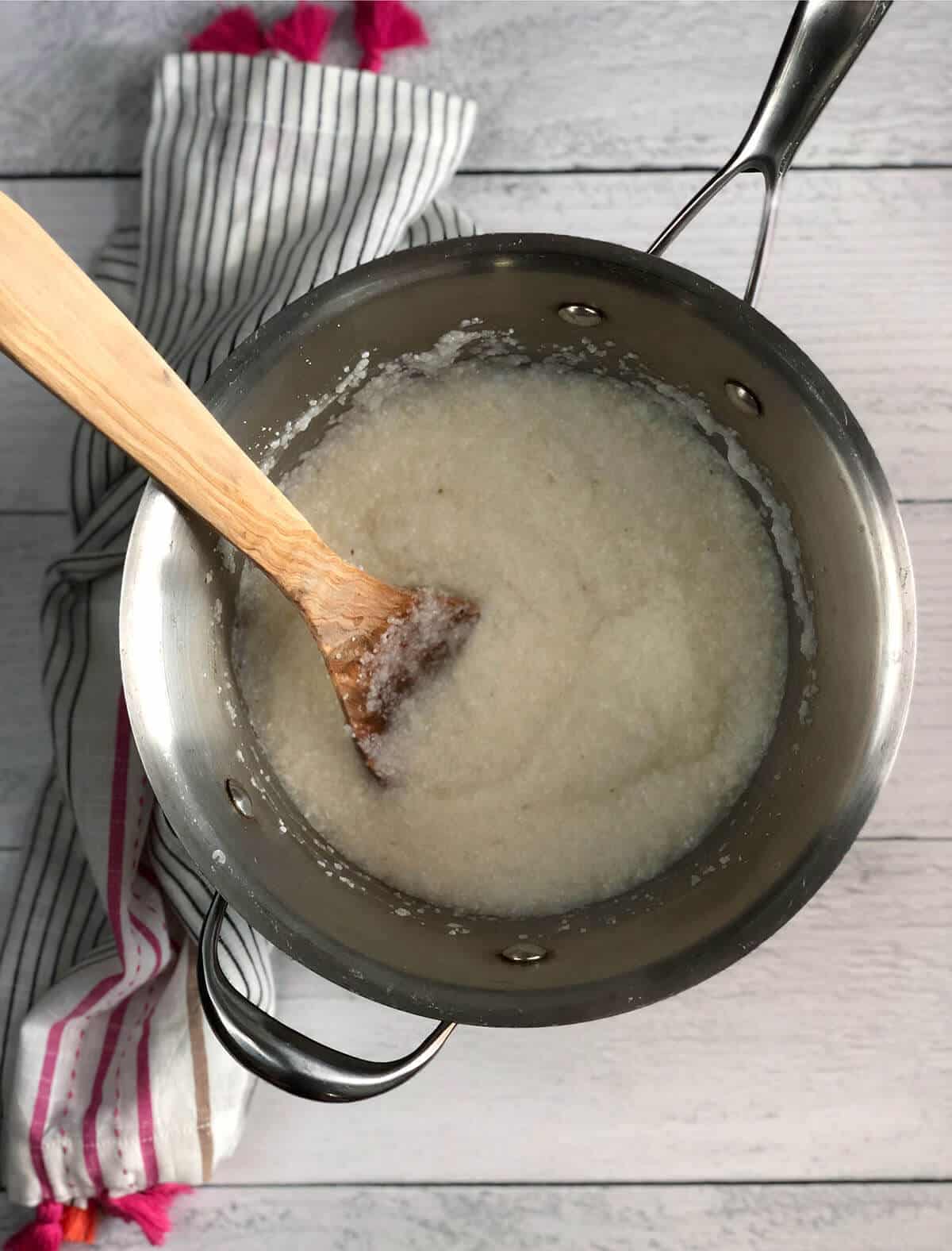 Wooden spoon stirring grits in a pot