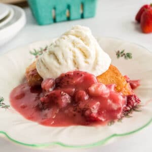 Strawberry cobbler topped with ice cream on a plate.